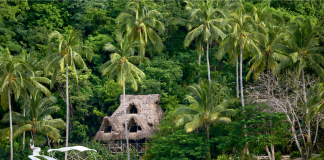 A yacht in front of a quiet sandy beach with a palapa