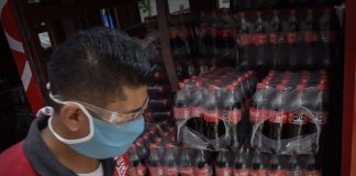 A man wearing a facemask unloads packages of plastic Coca Cola bottles from a truck