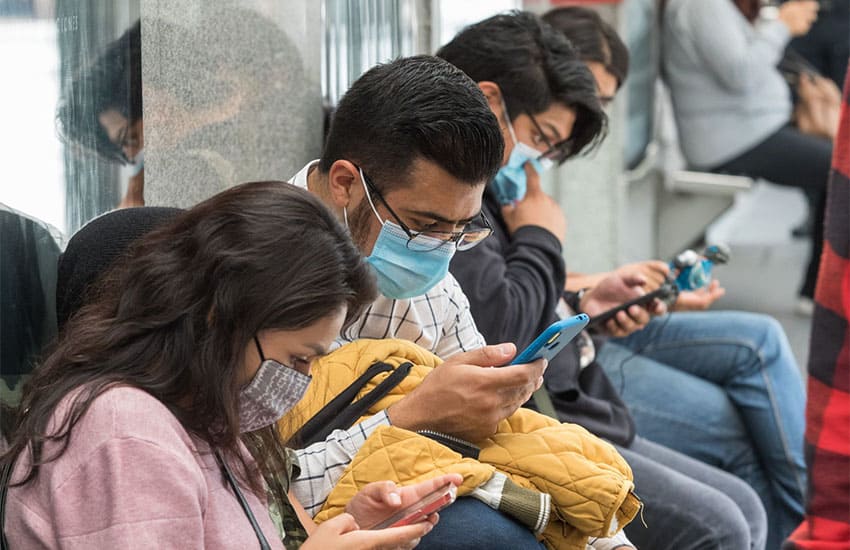 photo of Mexicans sitting at a bus stop using their cell phones
