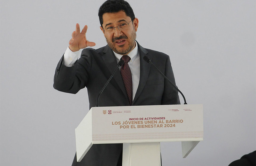 Mexico City Mayor Marti Batres standing at a podium gesturing with one hand in front of him.