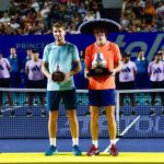 Alex de Miñaur and Casper Ruud pose on a tennis court with their respective first and second-place trophies
