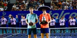 Alex de Miñaur and Casper Ruud pose on a tennis court with their respective first and second-place trophies