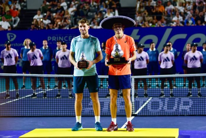 Alex de Miñaur and Casper Ruud pose on a tennis court with their respective first and second-place trophies