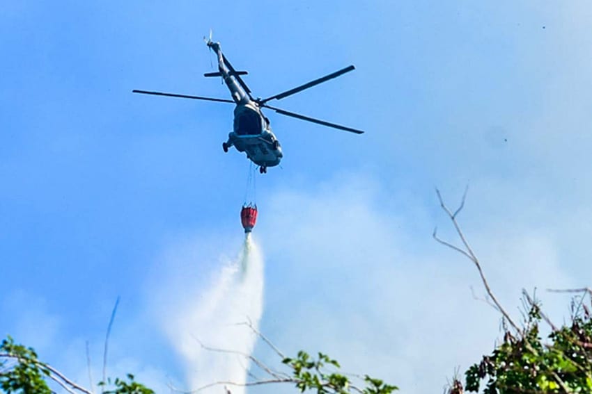 Firefighting helicopter dropping fire extinguishing chemicals over a forest
