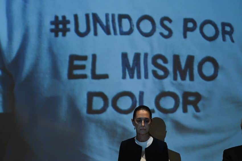 Mexico's presidential candidate Claudia Sheinbaum standing before a canvas sign stating "unidos por el mismo dolor"