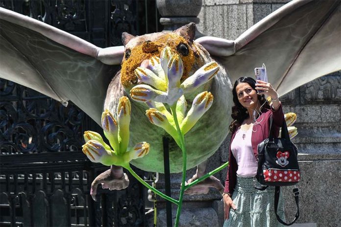 Mexican woman posing for a selfie with a larger-than-life display of a bat pollinating a plant