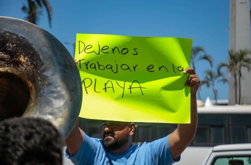 A musician holds a protest sign saying "Let us work on the beach"