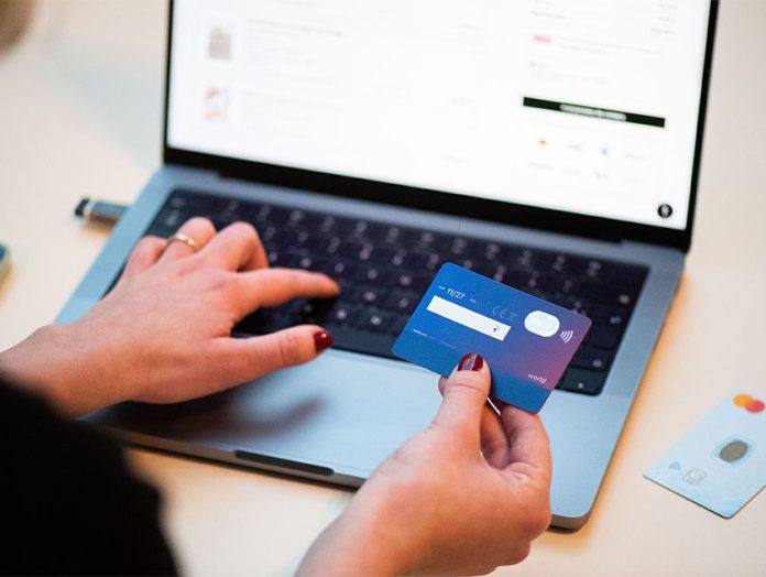 photo of a person's hands holding a credit card and entering information onto a laptop keyboard