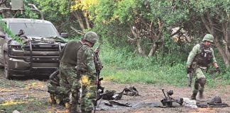 Soldiers look at spent explosives on a rural road, with their truck in the background.