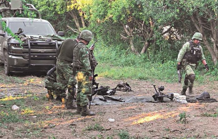 Soldiers look at spent explosives on a rural road, with their truck in the background.
