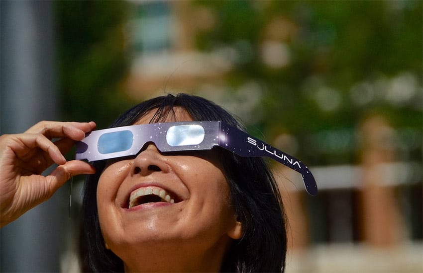 A woman wearing eclipse glasses looks up at the sky