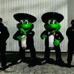 Two human-sized mariachi frog statues with police standing next to them