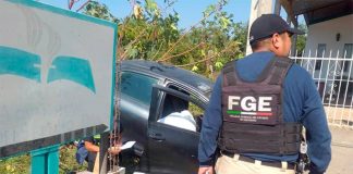 A man in a bullet-proof vest reading FGE in front of a crashed car