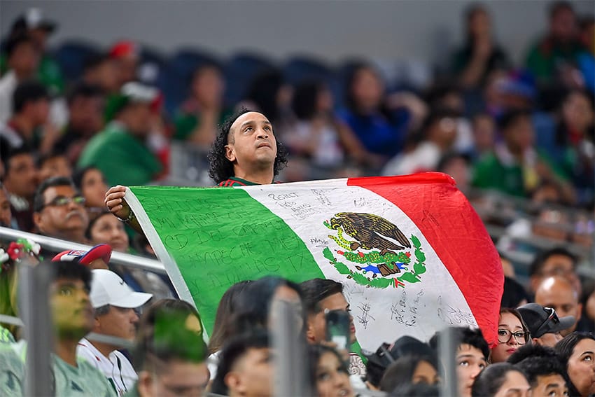 Un aficionado mexicano muestra una gran bandera mexicana en el campo de fútbol.
