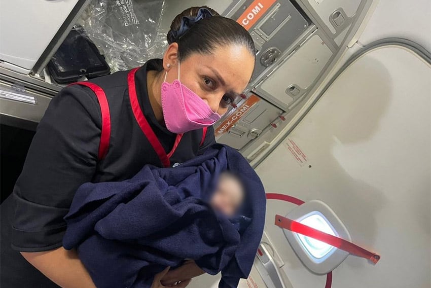 A flight attendant holds the baby, whose face is blurred for privacy.