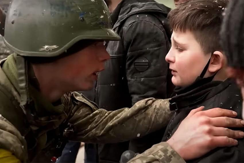Un hombre vestido con uniforme militar de combate estaba sentado con las manos sobre los hombros de un niño.