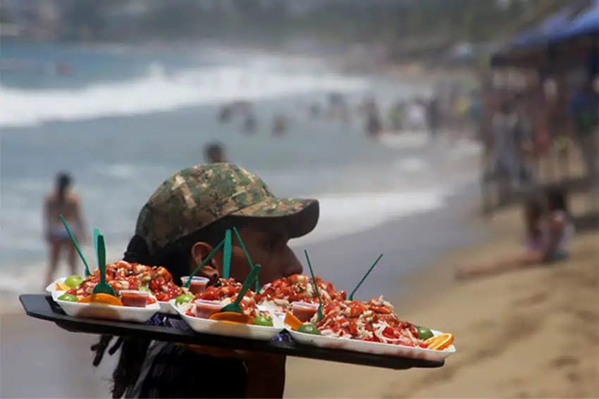 Vendor on Acapulco beach carrying tray of food items for sale
