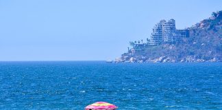 Acapulco beachgoer in front of ocean with damaged buildings in coastline view