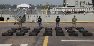 Mexican navy personnel standing with their backs to the camera in front of black bags on the ground.