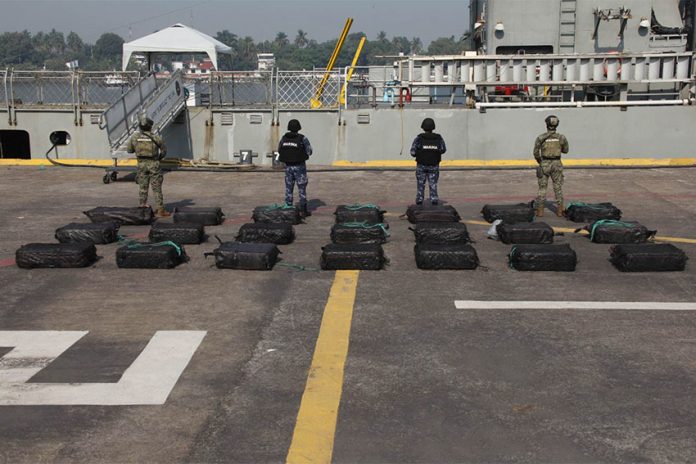 Mexican navy personnel standing with their backs to the camera in front of black bags on the ground.