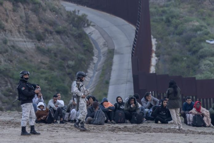 Members of Mexico's National Guard stand near migrants at the border with the United States