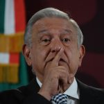 President Lopez Obrador at press conference with finger over his mouth as if calling for silence