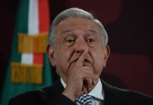 President Lopez Obrador at press conference with finger over his mouth as if calling for silence