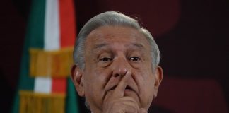 President Lopez Obrador at press conference with finger over his mouth as if calling for silence