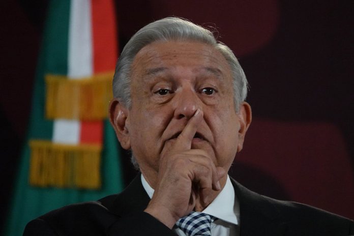 President Lopez Obrador at press conference with finger over his mouth as if calling for silence