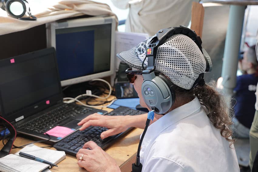 A woman wearing headphones and working on a laptop on a ship