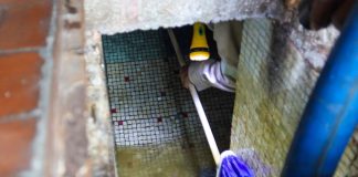 A person holds a flashlight and a broom as they clean out a well in Mexico City