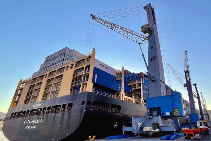 A cargo ship docked in with a crane preparing to remove containers