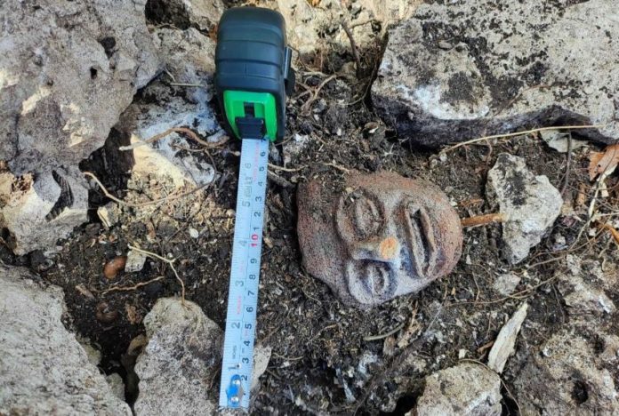 A mayan stone sculpture of a face, on the ground at a archeological dig in Chumpón, Mexico