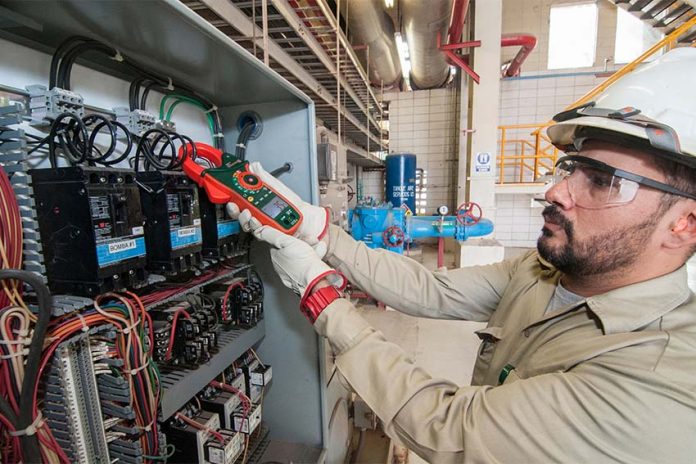 A Mexican electrician holding a digital monitor in front of a geothermal system