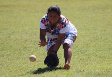 A Maya softball player wearing a traditional huipil pitches the ball.