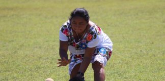 A Maya softball player wearing a traditional huipil pitches the ball.