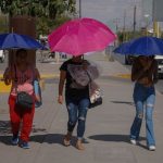 Three women shield themselves with umbrellas during a heat wave in Mexico.