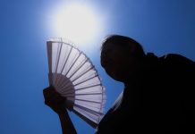 The sun shines above a woman holding a fan