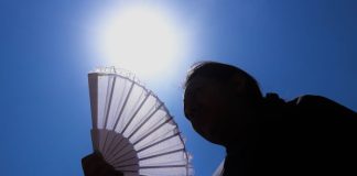 The sun shines above a woman holding a fan
