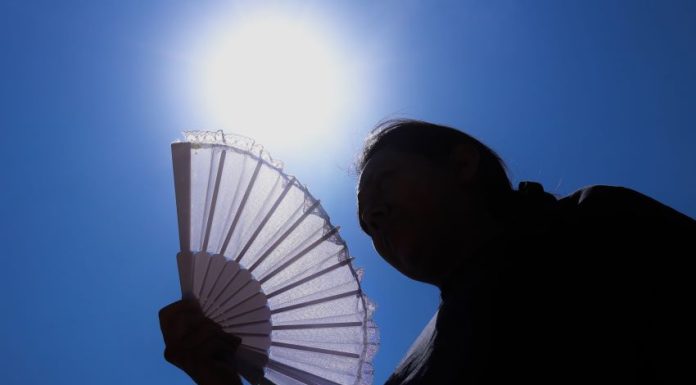 The sun shines above a woman holding a fan