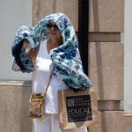 A middle-aged Mexican woman standing next to a building with a large blue and white scarf hanging over her head and shoulders to protect herself from high temperatures in Oaxaca city during a heat wave