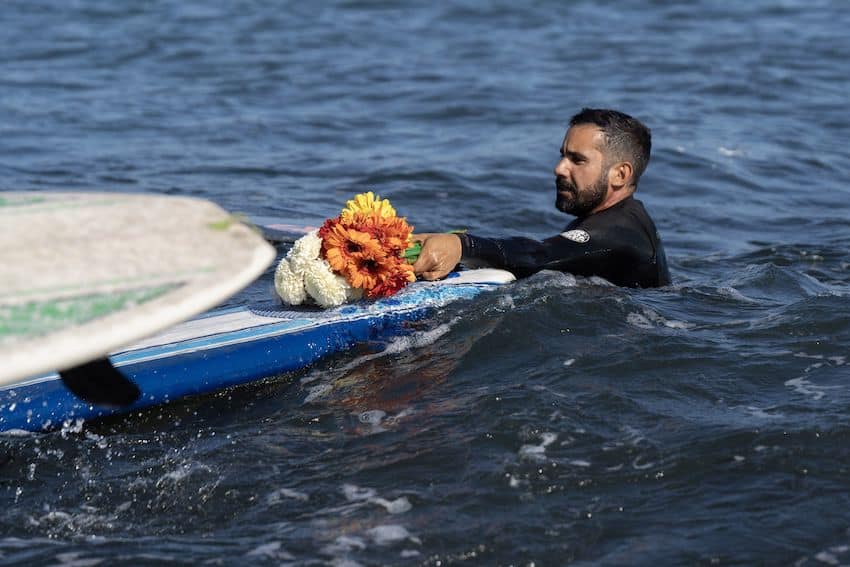 A surfer places flowers on a surfboard in memory of the three surfers kidnapped and killed in Baja California in late April 