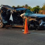 A mangled Ford SUV on a highway parked next to an orange highway cone