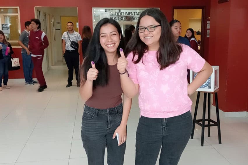 Two Mexican female college students on campus showing off their thumbs marked with indelible ink, proof that they voted in their university's mock presidential election