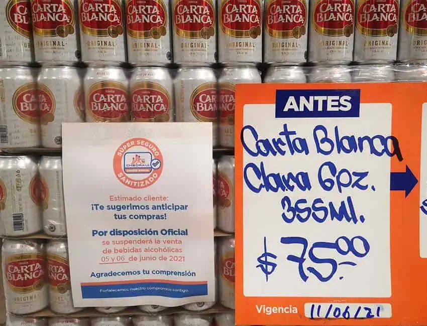 Stacked rows of Mexican beer cans with a cardboard sign announcing their price and another sign warning of an upcoming temporary alcohol sales ban