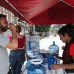 Man in Mexico City drinking a plastic cup of water at a hydration station during a heat wave.