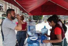 Man in Mexico City drinking a plastic cup of water at a hydration station during a heat wave.
