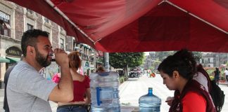 Man in Mexico City drinking a plastic cup of water at a hydration station during a heat wave.
