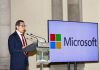 Mexico Finance Minister Rogelio Ramirez de la O standing at a podium beside a large monitor that bears the name and logo of Microsoft