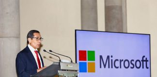 Mexico Finance Minister Rogelio Ramirez de la O standing at a podium beside a large monitor that bears the name and logo of Microsoft